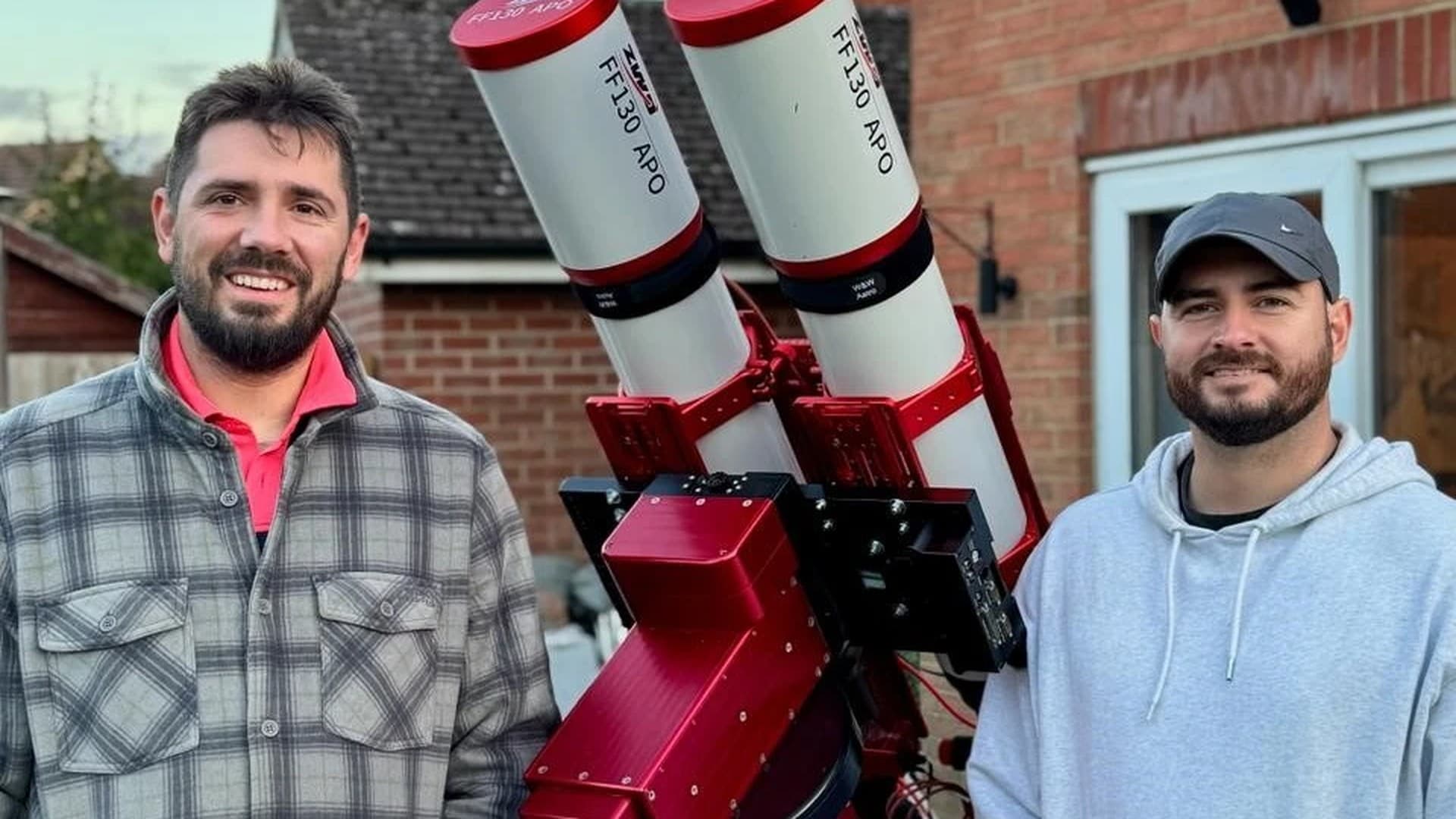 Phil and Jamie standing beside their twin ZWO FF130 APO refractors mounted on a red equatorial mount, assembled at home before shipping to Spain
