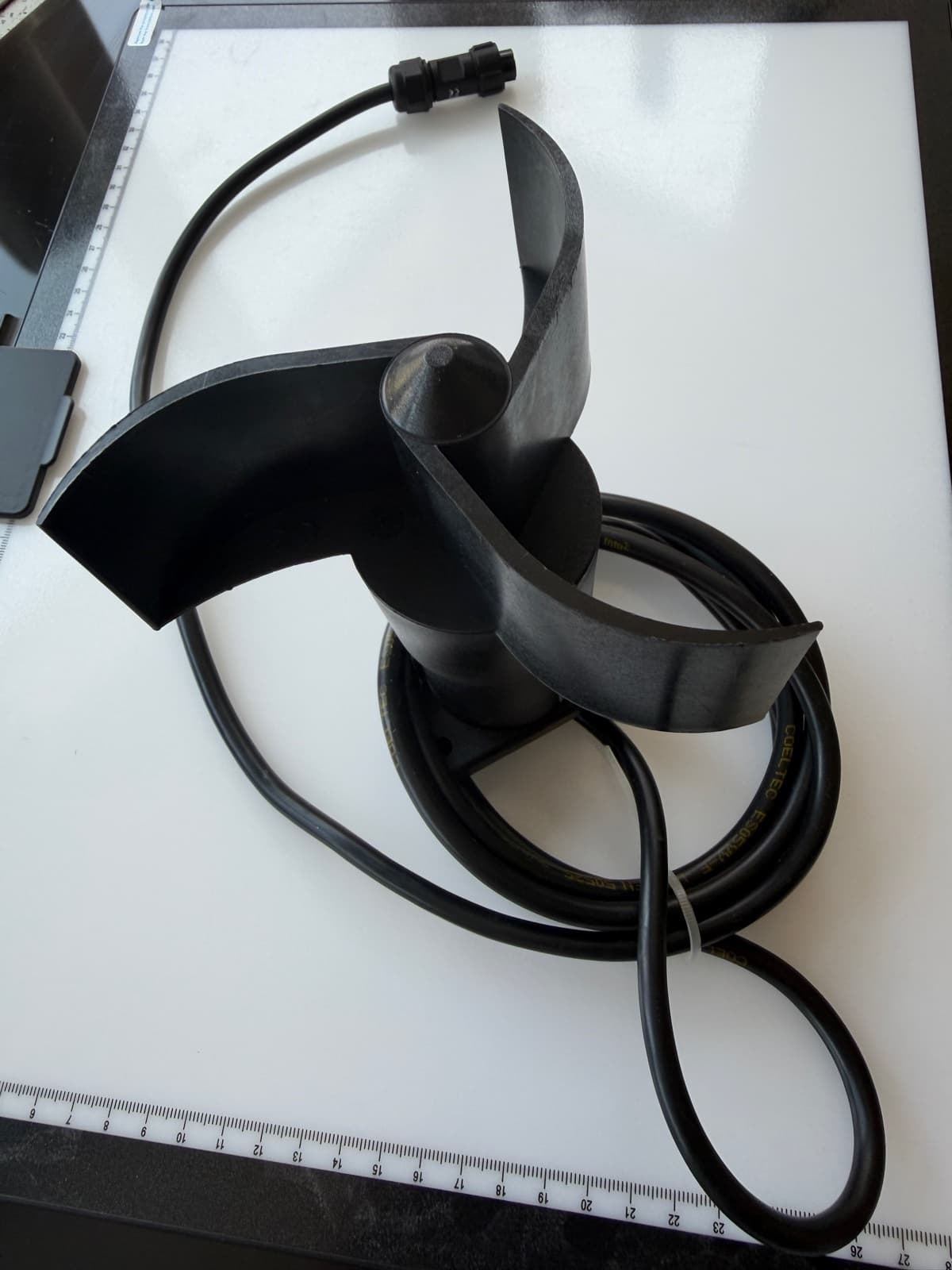 Black three-cup anemometer with its coiled cable and connector laid out on a light-coloured work surface.