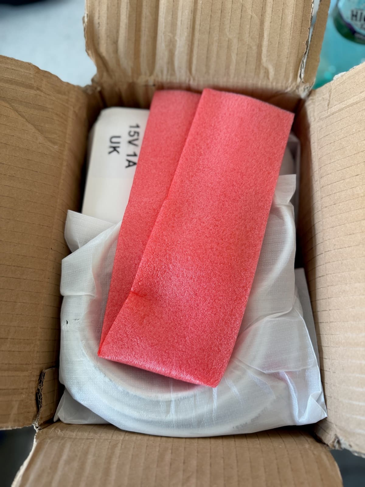 Open shipping carton containing white-wrapped equipment protected by red foam blocks.